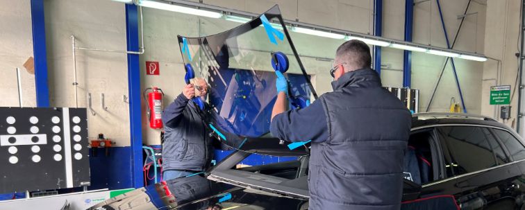 In einer Autowerkstatt setzen zwei Männer eine neue Windschutzscheibe ein.
